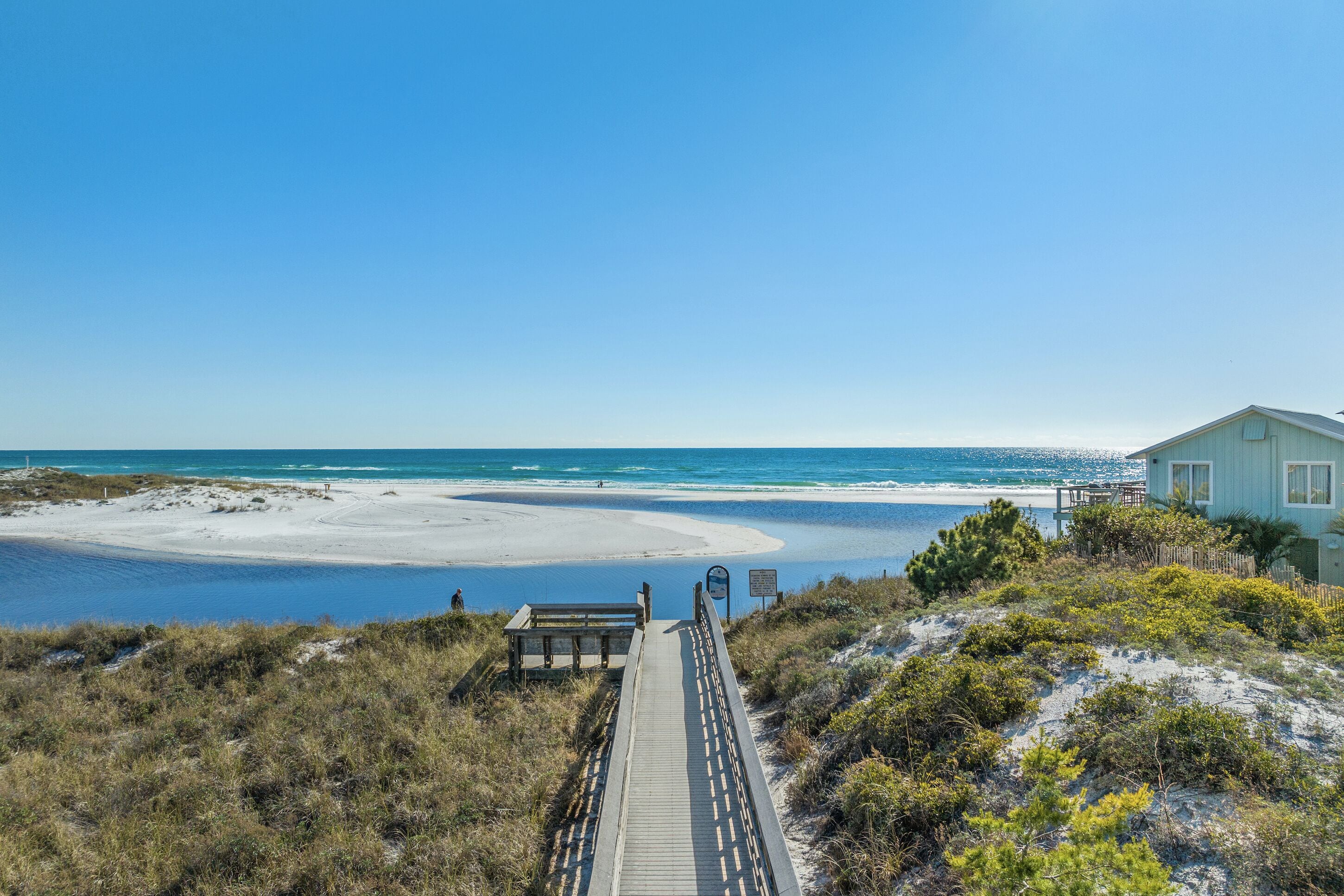 A beach with a wooden boardwalk leading to a house.