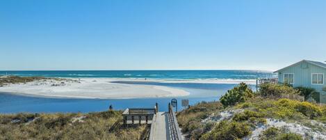A beach with a wooden boardwalk leading to a house.