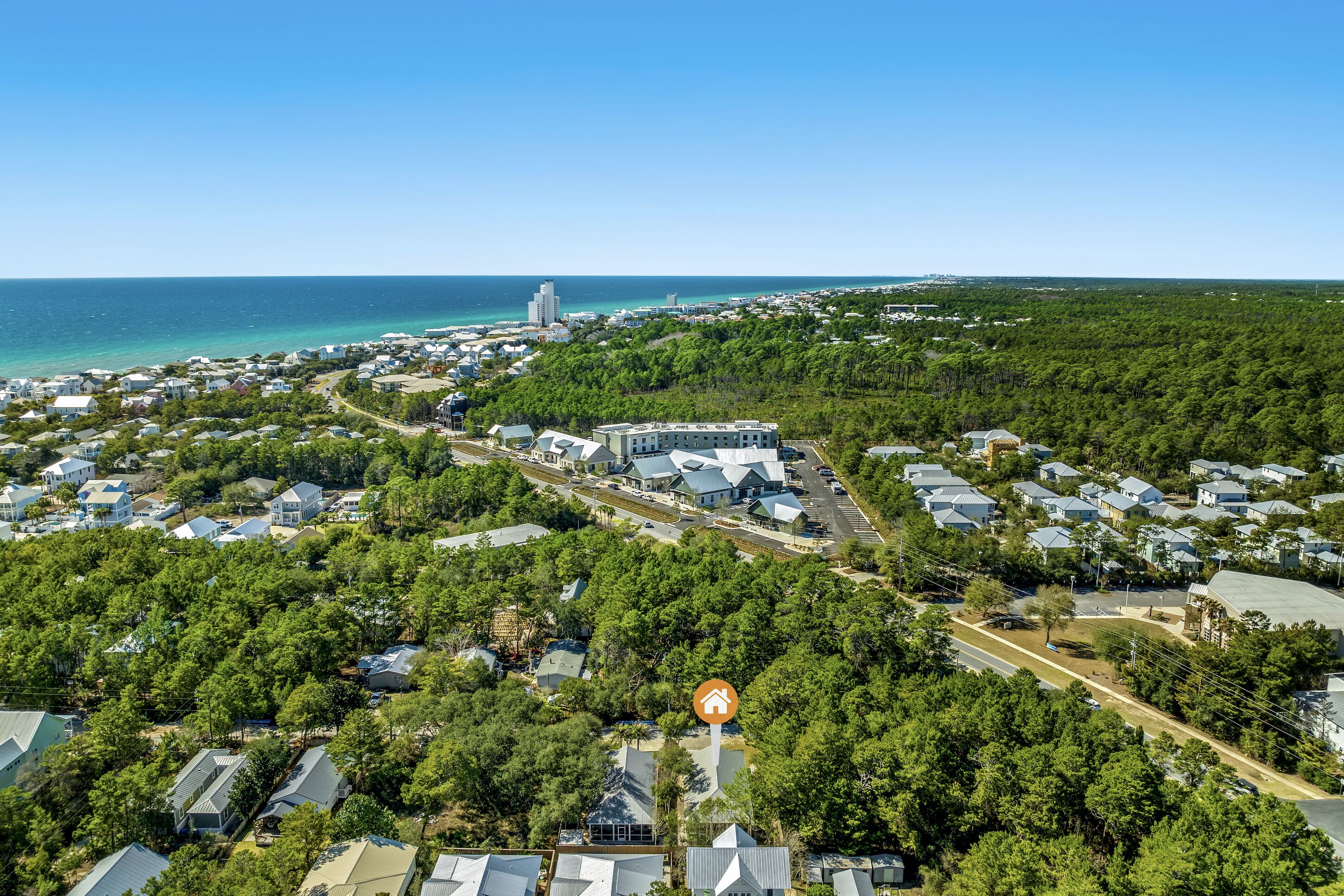 An aerial view of a coastal residential area with houses, a prominent building, and a clear view of the ocean.