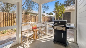 A covered patio with a grill, wooden chairs, and a table.