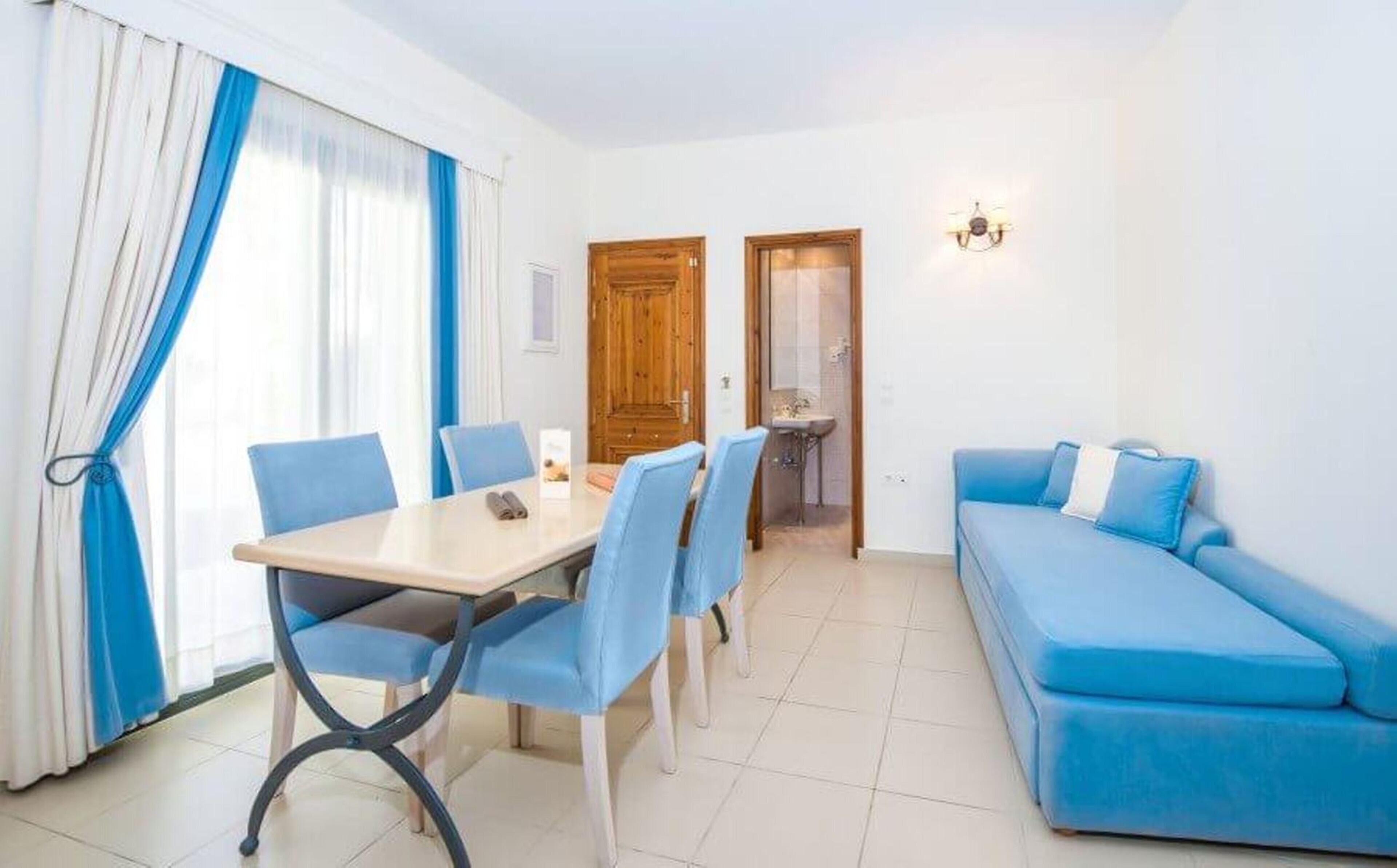 Een kamer met een eettafel en stoelen, een blauwe bank, een houten deur en een kleine badkamer.