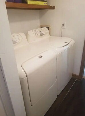 Una lavadora blanca en un cuarto de lavado, con un estante encima.