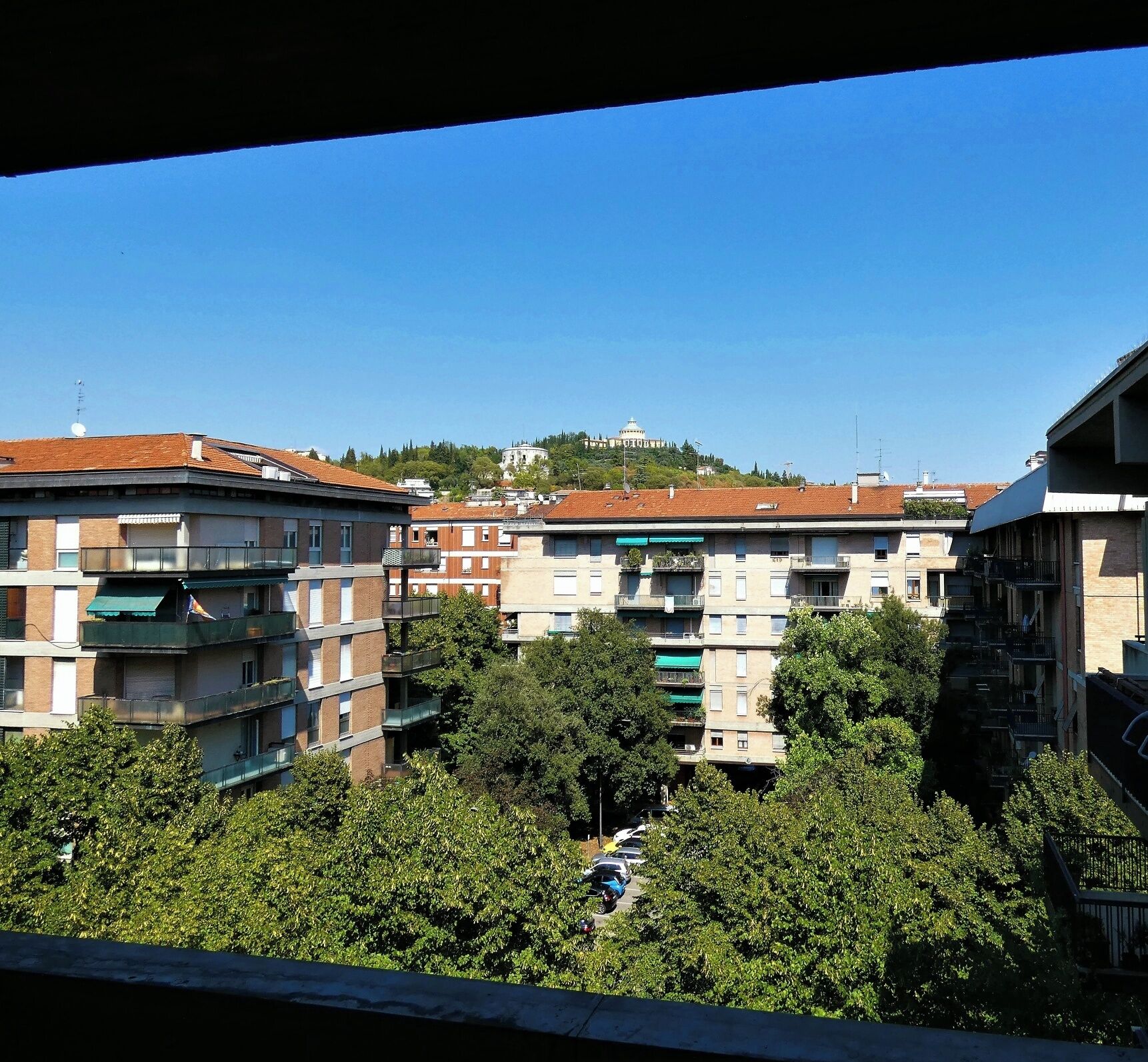 Un immeuble résidentiel à plusieurs étages, doté de balcons, entouré d’arbres et surplombant un ciel bleu clair.