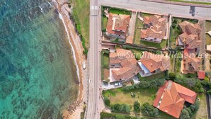Vue aérienne d’un quartier résidentiel situé sur la côte, avec des maisons dotées de toits recouverts de tuiles rouges, une route et un panneau de signalisation.