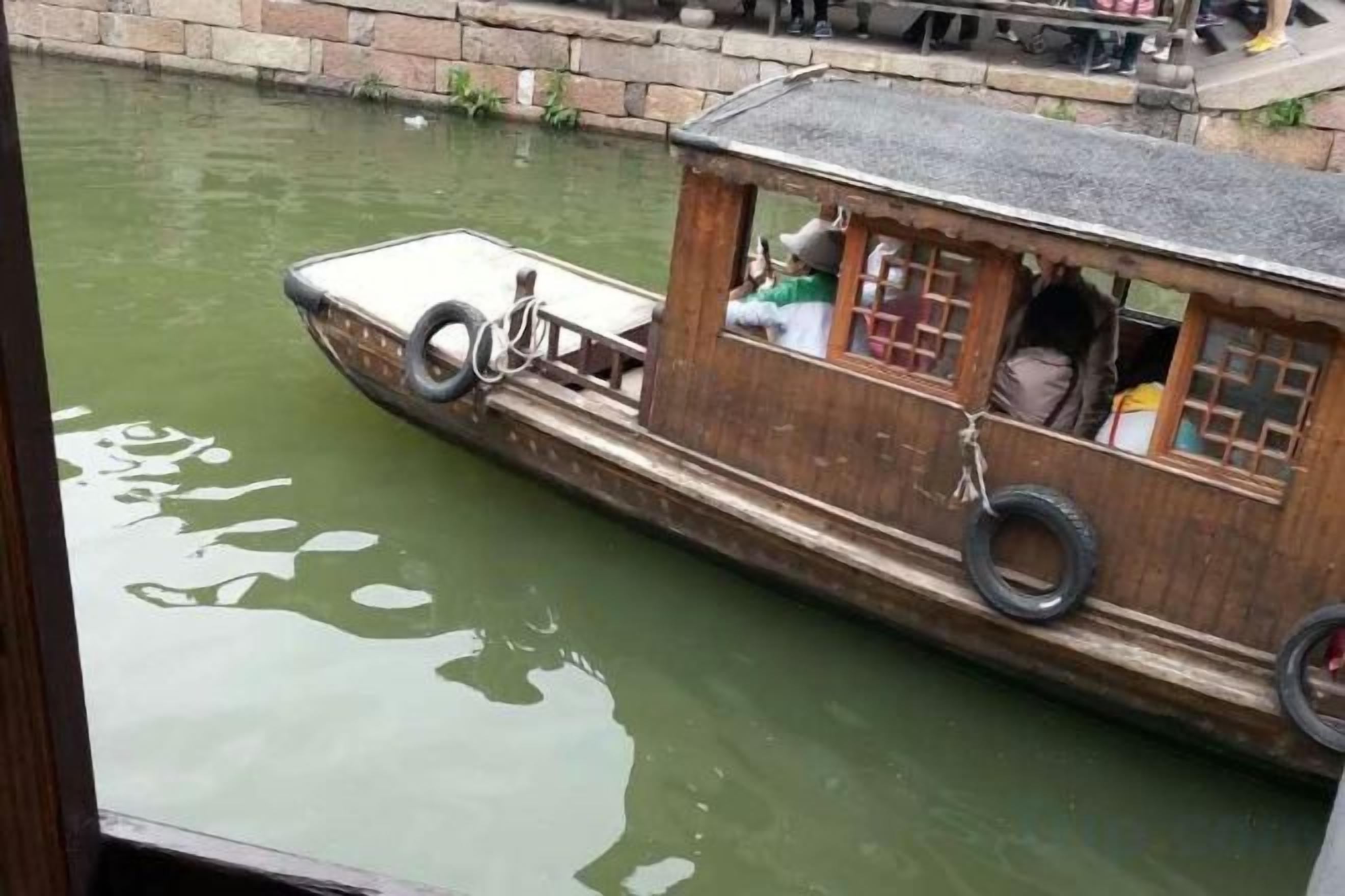 Une petite péniche à coque en bois, avec un pneu fixé sur le côté et une petite cabine.