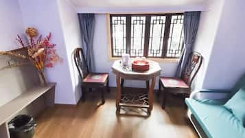 A room with a wooden floor, a table with chairs, a sofa, a window with curtains, and a vase with dried flowers.