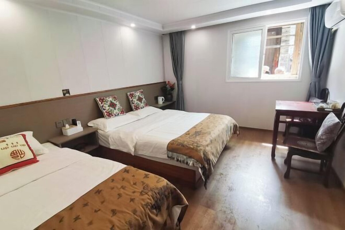 A hotel room with two beds, a desk, a chair, and a window with curtains.