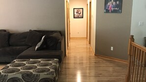 Un salon avec un plancher en bois, un canapé et un pouf à motifs.