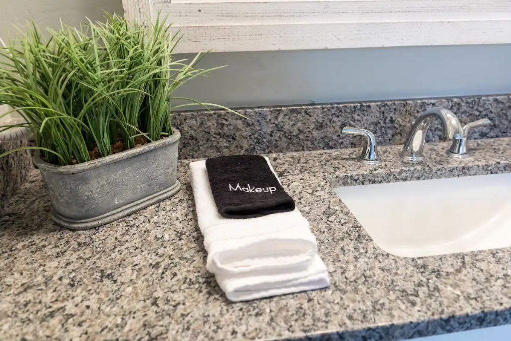 Une salle de bain avec un comptoir en granit, un lavabo, une plante en pot et une serviette pliée sur laquelle est écrit le mot « Maquillage ».