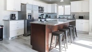 Una cucina moderna con mobili bianchi, elettrodomestici in acciaio inossidabile e un'isola centrale con sgabelli da bar.