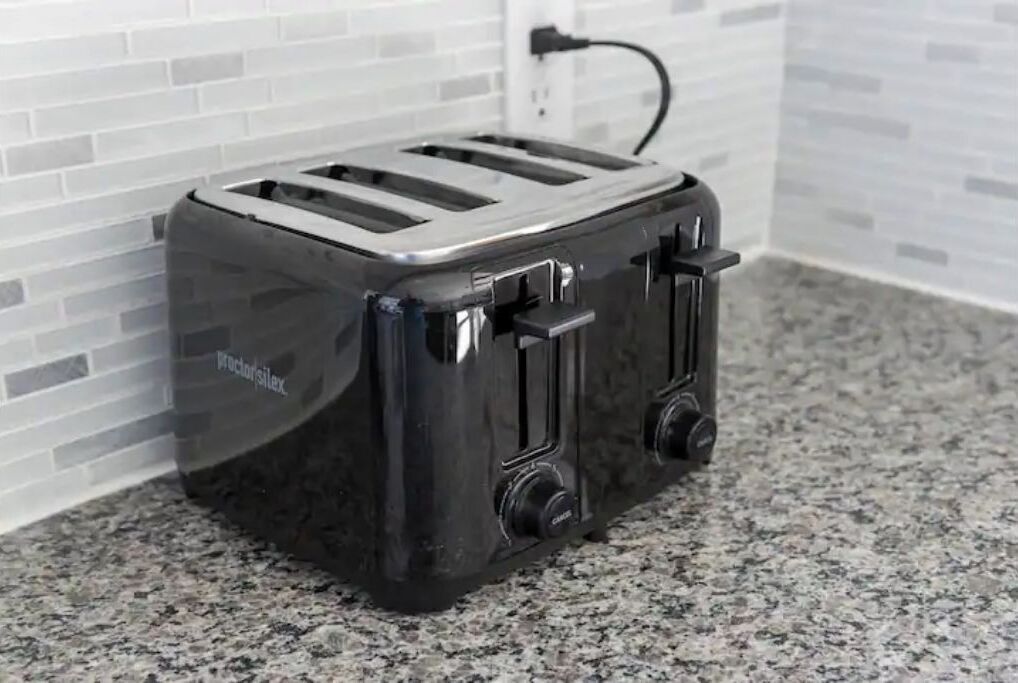 A black toaster with two slots and a power cord plugged in, placed on a granite countertop.