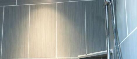 A modern shower with a handheld showerhead and a wall-mounted faucet.