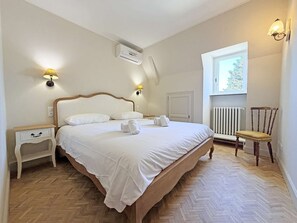 A bedroom with a bed, bedside tables, a radiator, a window, and a chair.