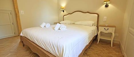 Una habitación de hotel con una cama grande, dos lámparas de noche, una mesita de noche de madera y un piso con estampado tipo espiga.