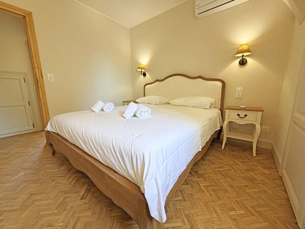 Una habitación de hotel con una cama grande, dos lámparas de noche, una mesita de noche de madera y un piso con estampado tipo espiga.
