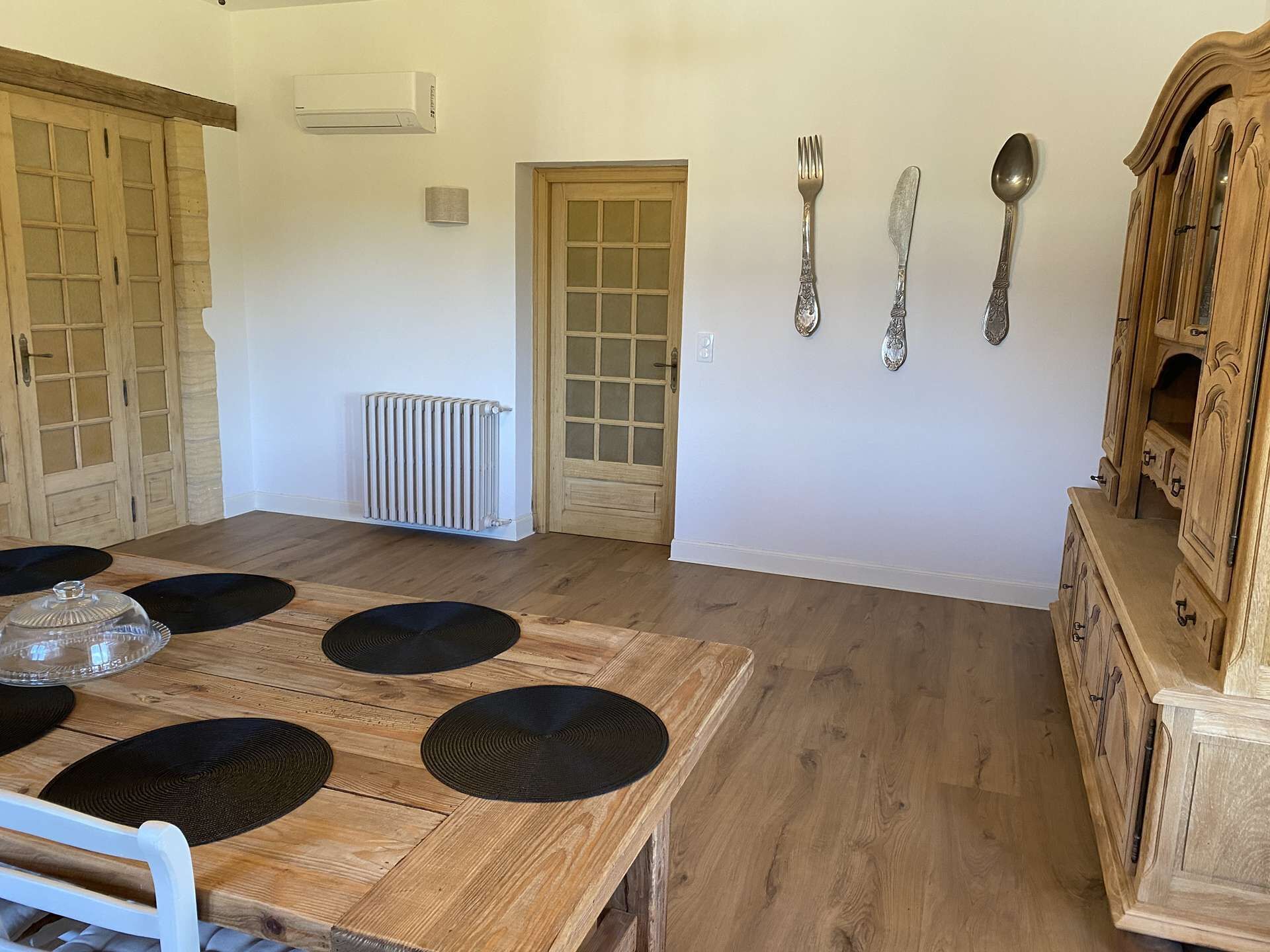 Zona de menjador amb taula de fusta, sotsplats negres i un armari d'estil antic.