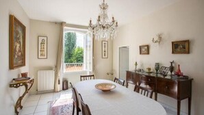 Une salle à manger avec une table ronde, des chaises, un lustre et une vue sur la verdure à l’extérieur.