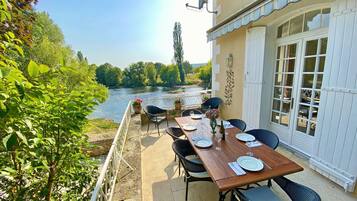 An outdoor dining area with a view of a river, surrounded by greenery.