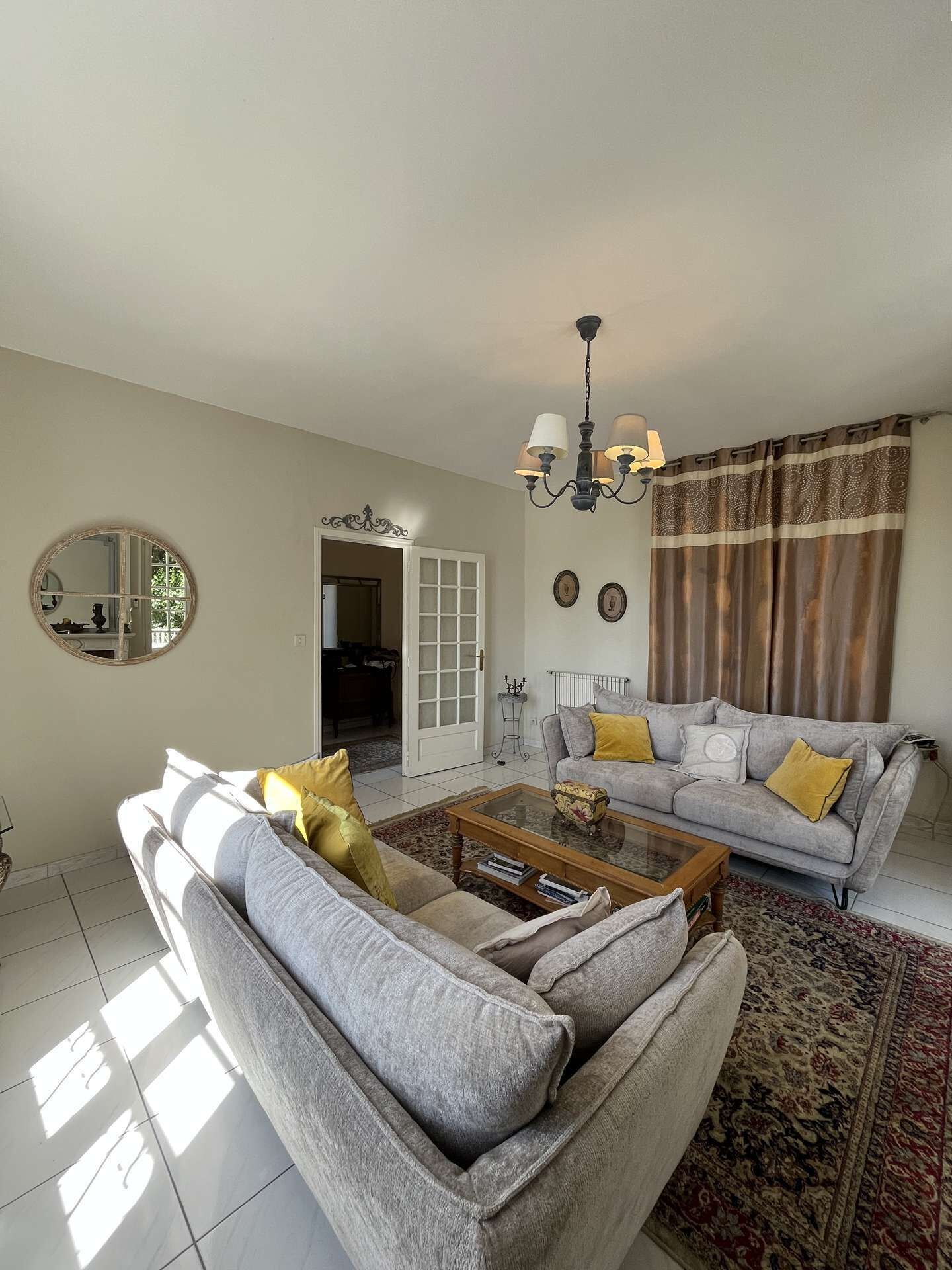 A living room with a grey sofa, a coffee table, a chandelier, and a patterned rug.