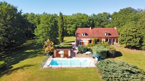 A two-story house with a swimming pool, surrounded by a well-maintained lawn and trees.
