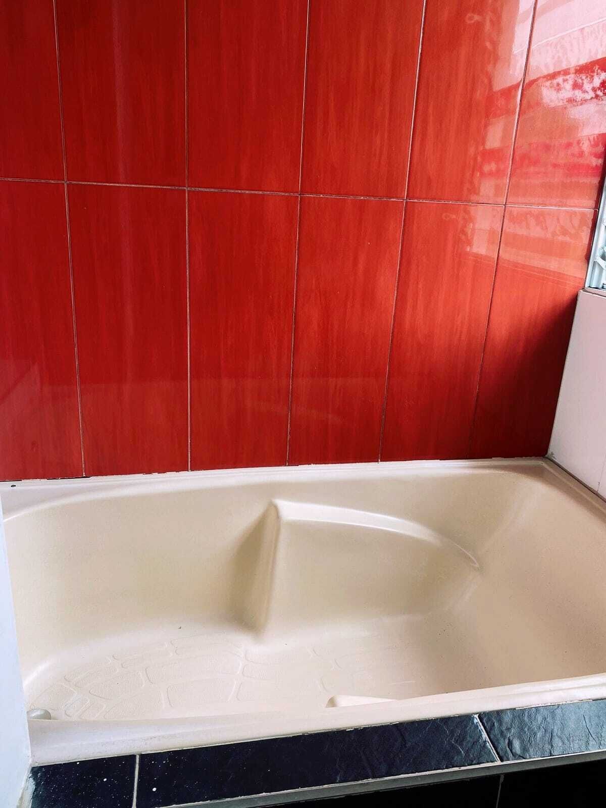 A bathtub with a white interior, red tiled walls, and a black tiled floor.