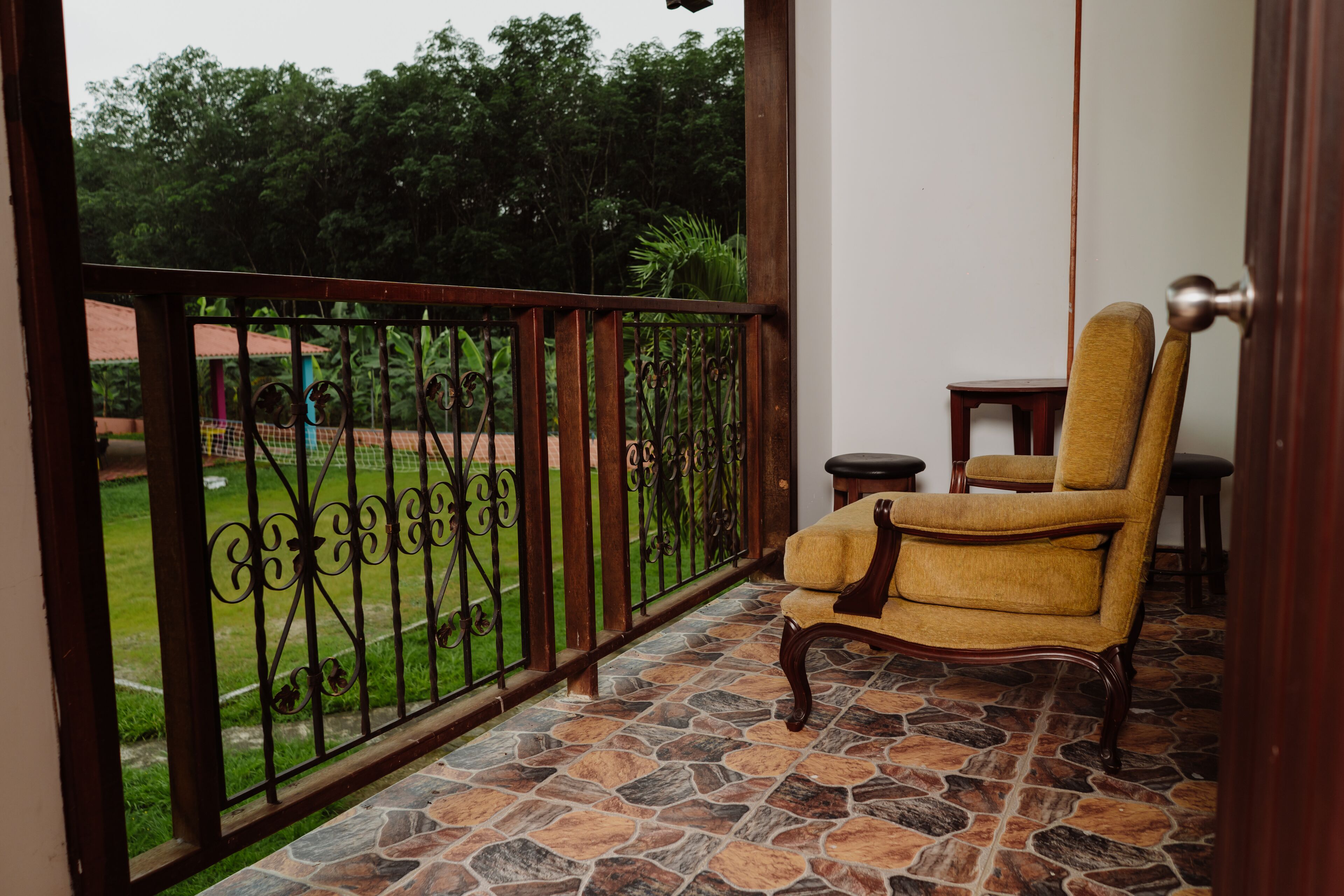 A balcony with a stone floor, a wrought iron railing, and a yellow armchair.