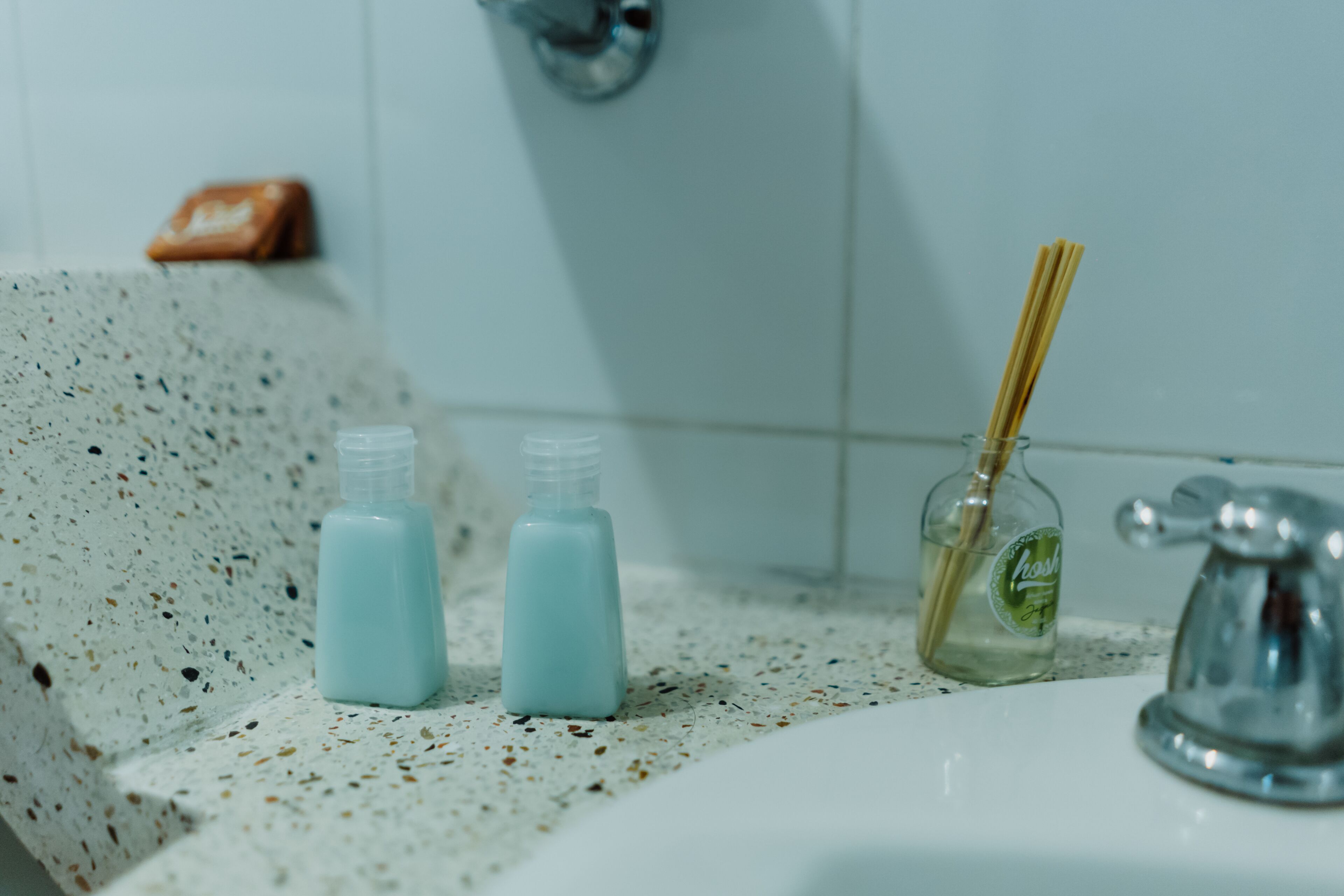 A bathroom sink with two bottles of liquid soap and a bottle of reed diffuser.