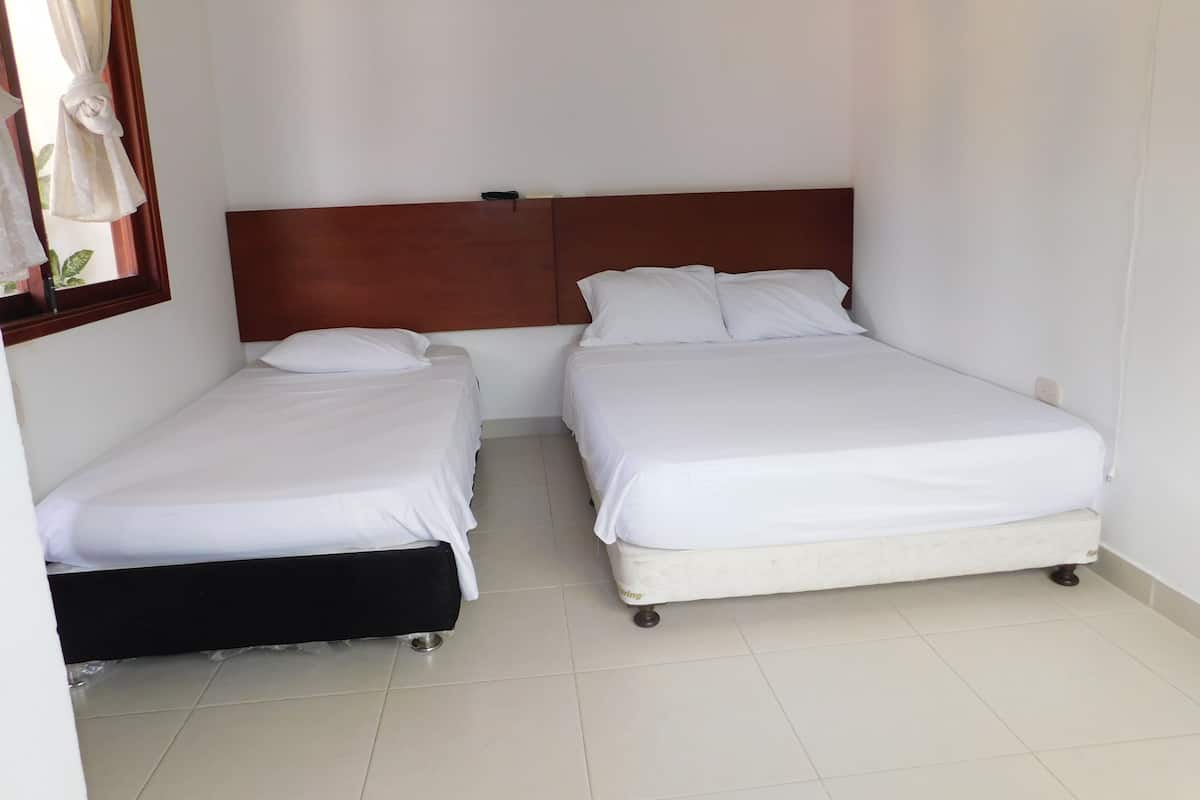 Ett hotellrum med två separata sängar, en sänggavel i trä, vita sängkläder och ett klinkergolv.