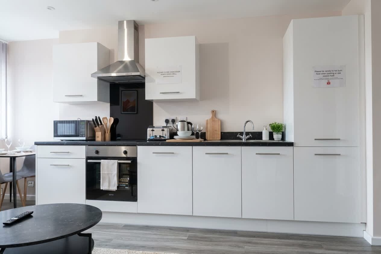 Una cocina moderna con armarios blancos, una campana extractora de acero inoxidable, un microondas, un tostador y un lavabo.