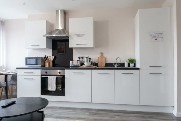 A modern kitchen with white cabinets, a stainless steel range hood, a microwave, a toaster, and a sink.