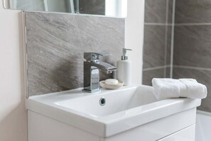 Ein Badezimmer mit einem weißen Waschbecken, einem modernen Wasserhahn, einer Seifenspender und einem Handtuch auf der Ablagefläche.