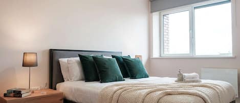 A bedroom with a bed, bedside table, lamp, and a window with blinds.