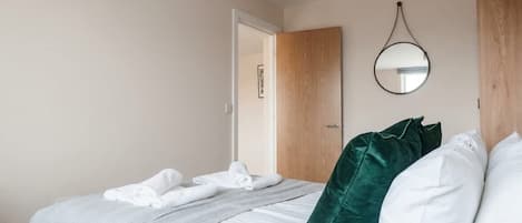 Un lit bien fait, avec du linge de lit blanc, un coussin vert et un miroir rond accroché au mur.