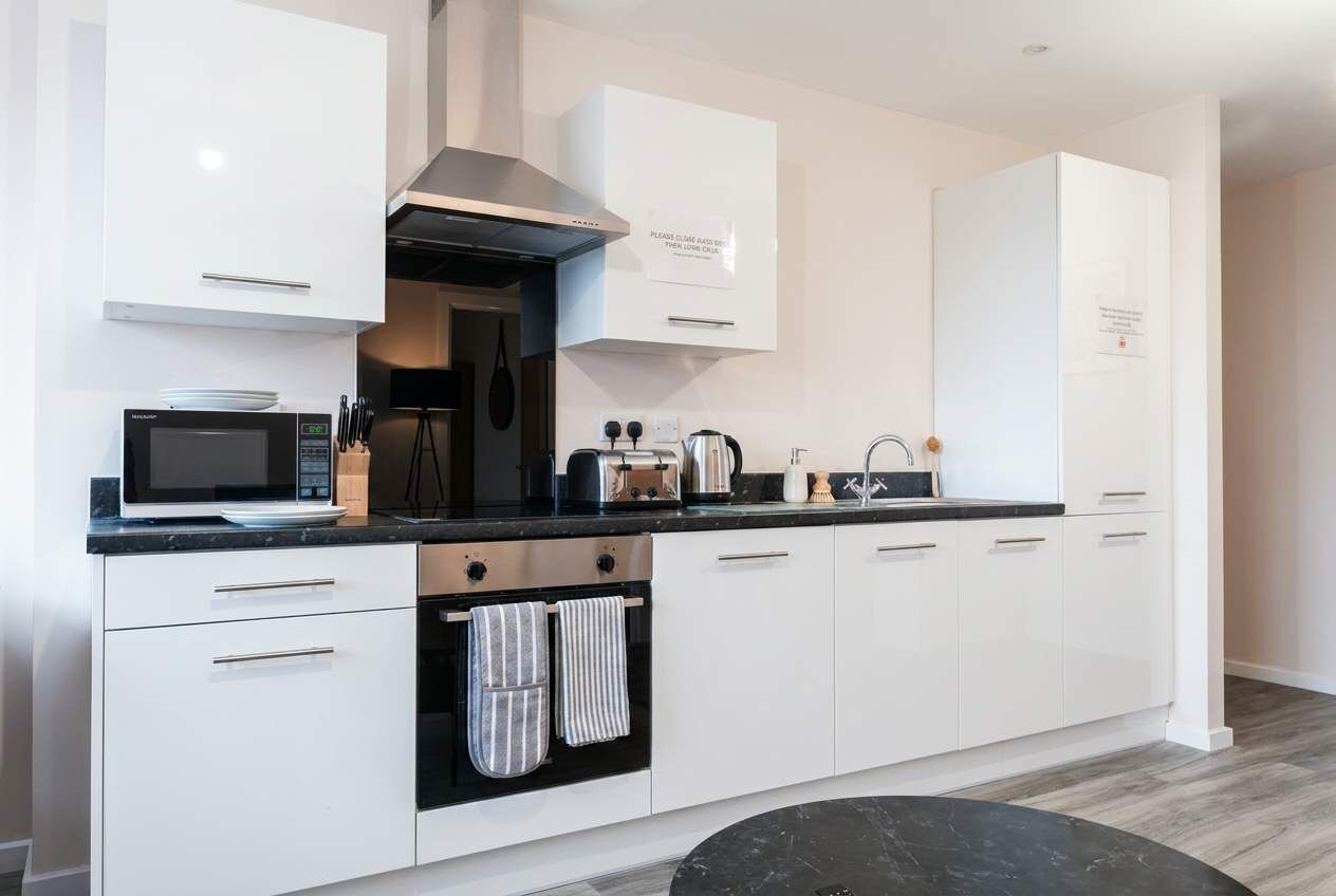 A modern kitchen with white cabinetry, a built-in oven, a microwave, and a stainless steel range hood.