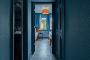 A narrow hallway leading to a bedroom with a bed, a nightstand, and a window with curtains.