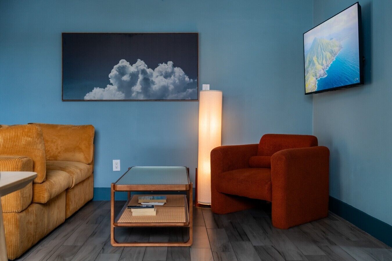 A room with a blue wall, a wooden floor, a sofa, a coffee table, a floor lamp, and two framed pictures.