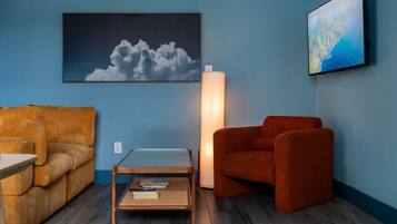 A room with a blue wall, a wooden floor, a sofa, a coffee table, a floor lamp, and two framed pictures.