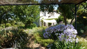 Ein Garten mit einem weißen Haus, einer Holzbank und einer Pergola.