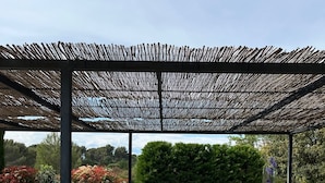Ein Essbereich im Freien mit einer Steigetheke, Metallstühlen und einer Pergola darüber.