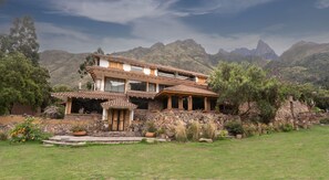 A two-story house with a stone facade, a tiled roof, and a patio area with potted plants. - Casa Raiz -The Handmade House in Calca (Calca)