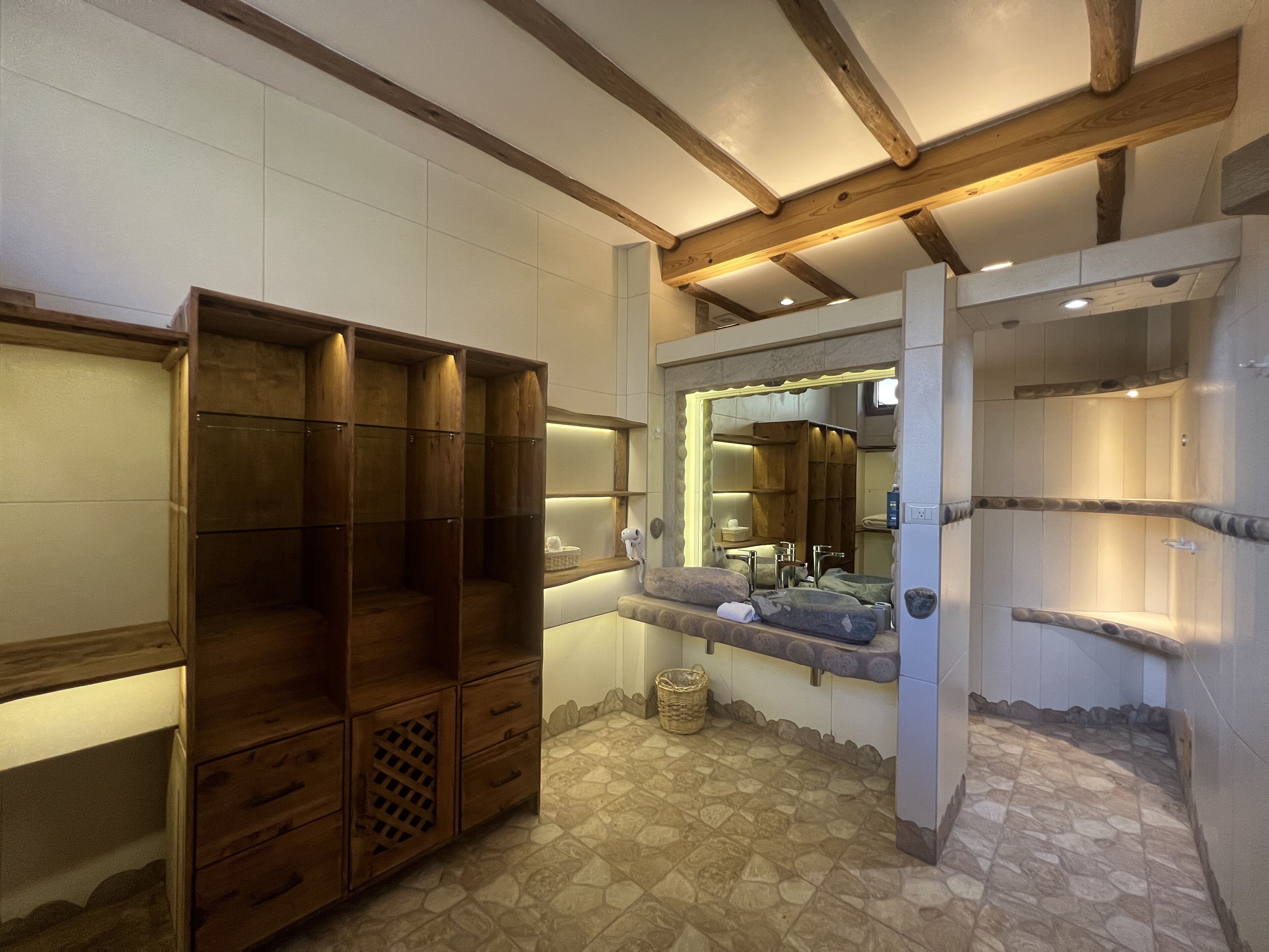 Une salle de bain avec un meuble-lavabo en bois, un miroir et un sol carrelé en pierre.