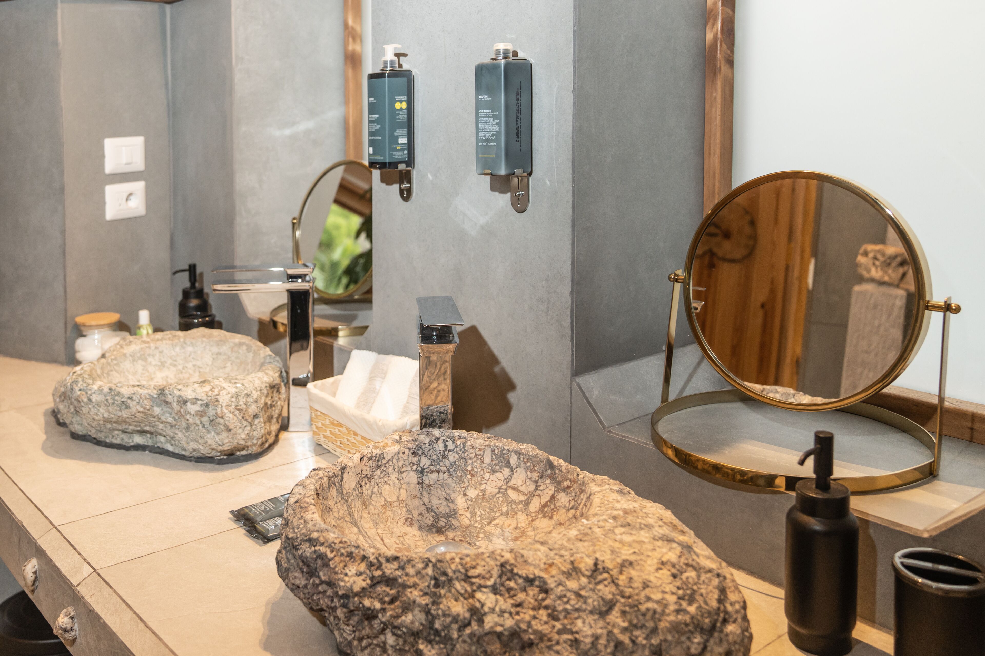 A bathroom with a granite sink, a round mirror, and two wall-mounted soap dispensers.