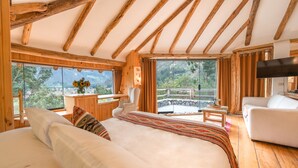 A bedroom with a large bed, a desk, a chair, and a TV. There is a balcony with a view of the outdoors. - Casa Raiz -The Handmade House in Calca (Calca)