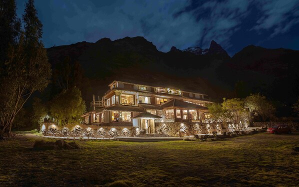 A multi-story building with a stone facade, large windows, and a balcony overlooking a landscaped area. - Casa Raiz -The Handmade House in Calca (Calca)