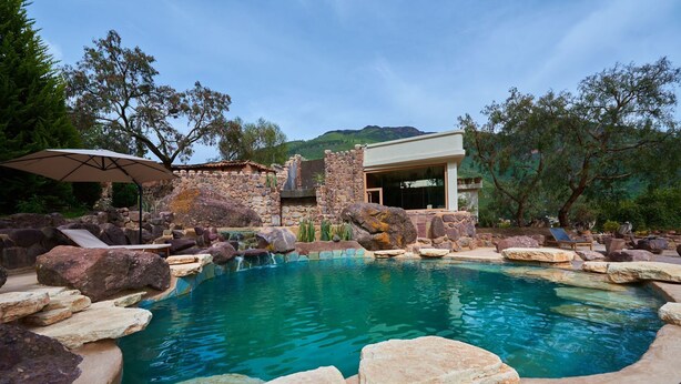A pool surrounded by rocks and a stone building with a glass door. - Casa Raiz -The Handmade House in Calca (Calca)