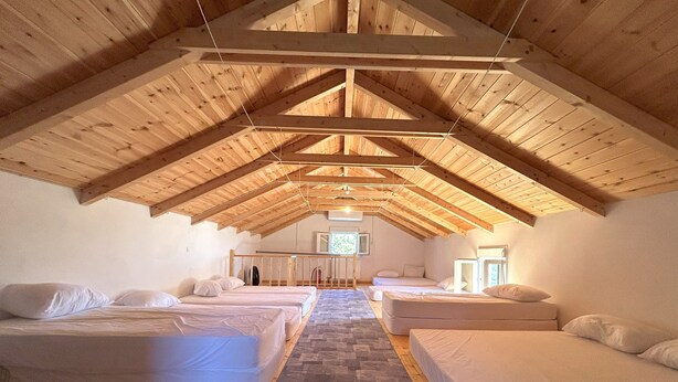 Une chambre confortable située sous les toits, avec des poutres apparentes, deux lits, une télévision et une petite fenêtre.