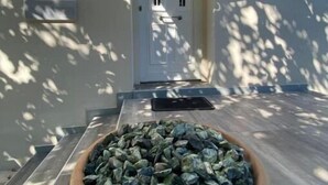 Une entrée de maison avec une porte blanche, un pot de fleurs décoré de pierres et un plancher en bois.