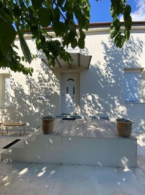 Un patio con una puerta blanca, dos plantas en macetas y una pequeña mesa.