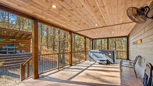 Een houten terras met een barbecueplaats, een ventilator en uitzicht op het bos.