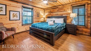 Een slaapkamer met een houten plafond, een bed met een donker hoofdeinde, een nachtkastje en een stoel.